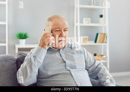 Uomo anziano che ha Una conversazione telefonica seria sul divano nel soggiorno Foto Stock