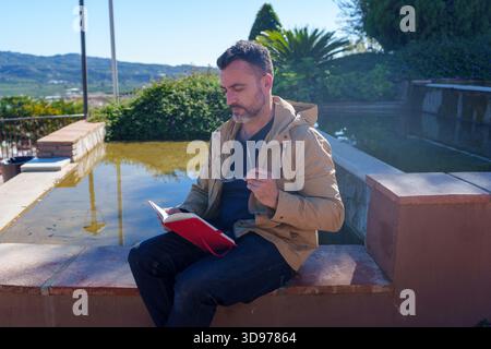 Uomo che legge un diario all'aperto, concentrandosi su pensieri e idee mentre si gode un momento di pace nella natura Foto Stock