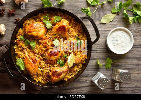 Deliziosi biriyani di pollo fatti in casa serviti in una padella di ghisa su sfondo di legno scuro. Piatto indiano tradizionale. Vista dall'alto, disposizione piatta Foto Stock