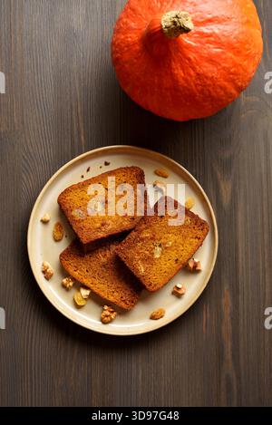 Fette di pane di zucca con uvetta e noci sul piatto su fondo marrone in legno. Vista dall'alto, disposizione piatta Foto Stock