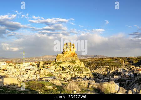 Vista dell'antico castello di Ortahisar arroccato sulla cima di una collina, circondato da tradizionali case in pietra sotto un vasto cielo blu, Ortahisar, Cappadocia, Turchia. Foto Stock
