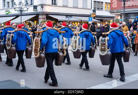 Winterthur, Svizzera - 30 novembre 2025: Sfilata festosa con i partecipanti in giacche blu e cappelli rossi che trasportano grandi campane di mucca decorate, Foto Stock