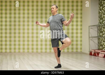 Tenere in posa l'albero adulto uomo caucasico in equilibrio in una sala fitness interna di fronte allo specchio migliorando la stabilità la concentrazione e l'allineamento del corpo dopo il lavoro Foto Stock