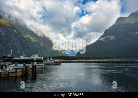 Vista panoramica di Milford Sound con porto, barche da visita, paesaggio di montagna e cielo nuvoloso nel parco nazionale di Fiordland, nuova Zelanda Foto Stock