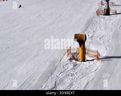 Cannone da neve giallo su una pista da sci con rete di sicurezza Foto Stock