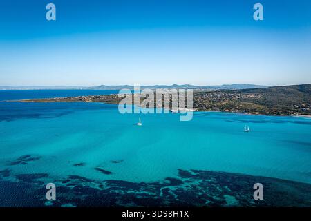 Vista aerea del mare turchese che incontra una costa frastagliata, piccole barche a vela che volano in acque calme, Sardegna, Italia Foto Stock