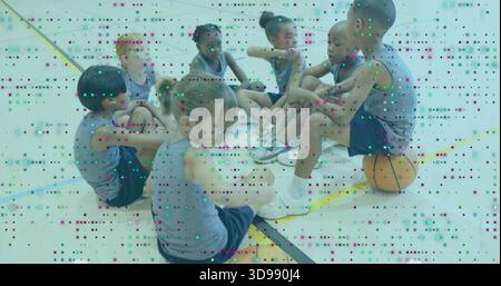 Sette bambini seduti in maglie grigie che parlano sul pavimento della palestra con pallacanestro arancione, linee dipinte Foto Stock