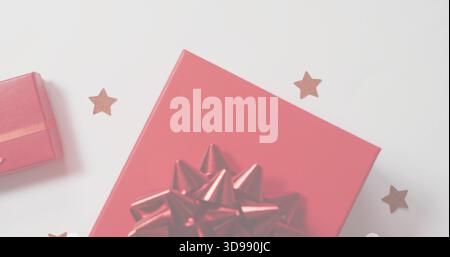 Grande confezione regalo rossa su tavolo bianco, con fiocco lucido, piccola scatola rossa, coriandoli stellati Foto Stock