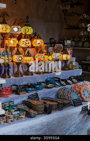 Una bancarella espone una varietà di colorate lampade a mosaico turco artigianali e ciotole in ceramica, probabilmente in un mercato o in un festival, invitando gli acquirenti alle sopracciglia Foto Stock