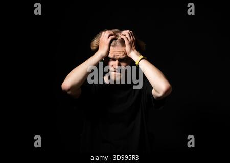 Uomo stressato che tira i capelli con frustrazione su sfondo scuro, emozionante ritratto in studio Foto Stock
