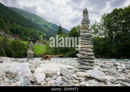 Un'alta torre di pietre impilate si erge sul fiume a Praegraten in Austria in una nuvolosa giornata estiva creando una scultura naturale. Foto Stock