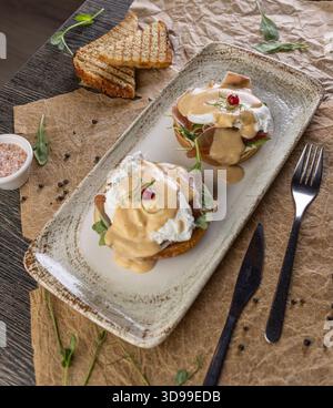 Uova benedict con uova in camicia, prosciutto e salsa hollandaise sul tavolo del ristorante Foto Stock
