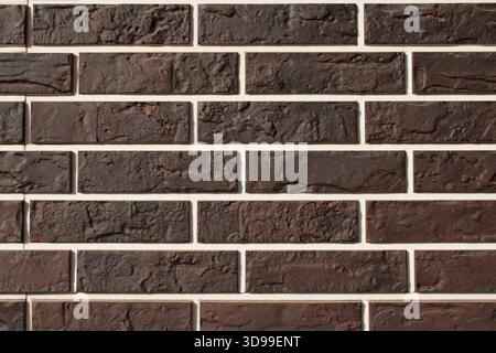 Una parete di mattoni marroni fatta di vari mattoni scuri e chiari disposti in un motivo orizzontale. Il muro è dritto con un aspetto pulito. Foto Stock