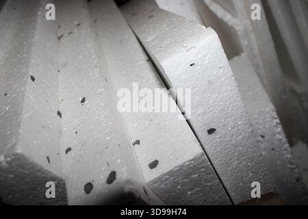 I pezzi in schiuma bianca sono impilati insieme in un'area di lavoro. Sono utilizzati per vari scopi, come isolamento o imballaggio. I pezzi hanno una piccola spe scura Foto Stock