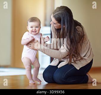 Mamma, bambina e cammina sul pavimento in casa, imparando o legando con cura, amore o sostegno al mattino. Donna, mamma e bambino con i gradini, sorridi Foto Stock