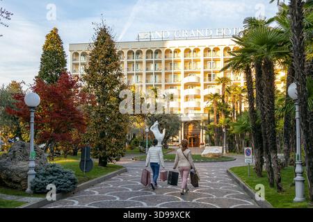 Abano Terme, Italia - 28 ottobre 2025: Ospiti che camminano verso l'ingresso dell'Abano Grand Hotel portando con sé le borse della spesa Foto Stock