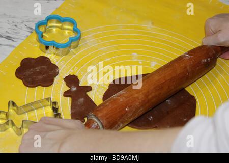 Si vedono le mani che rotolano l'impasto su una superficie gialla. Accanto all'impasto arrotolato si trovano diverse forchette di forme diverse. Questa scena mostra un'azione di cottura al forno Foto Stock