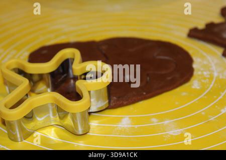 Una persona sta stendendo l'impasto marrone su una superficie gialla mentre utilizza una forchetta a forma di stella. La farina viene sparsa durante il processo di cottura. Foto Stock