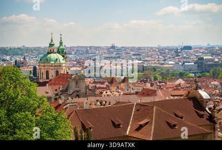 Vista mozzafiato del paesaggio urbano storico di Praga con cupole verdi, tetti di tegole rosse e guglie gotiche sotto un cielo luminoso e limpido. Un vivace cittadino europeo Foto Stock