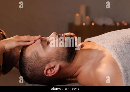 Primo piano di un uomo che riceve un massaggio alla testa e si rilassa con gli occhi chiusi nella spa. , concetto di massaggio Foto Stock