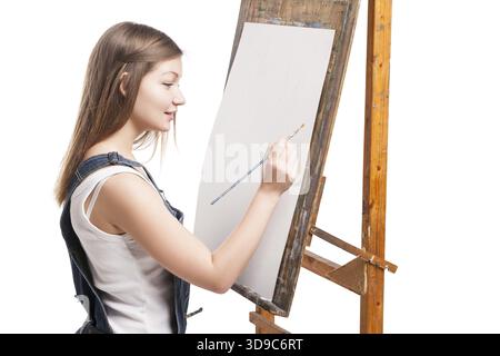 Donna sorridente pittrice con pennello seduta a cavalletto che disegna con vernici acriliche Foto Stock