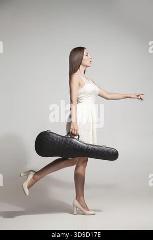 Vista laterale del musicista femmina in abito bianco azienda nero violino caso.Studio shot Foto Stock