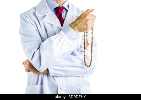 Maschio caucasico medico vestito in camice bianco, blu camicia e cravatta rossa è in legno di contenimento i grani del Rosario con la mano destra Foto Stock