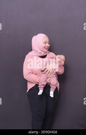 Una madre che indossa un hijab e un maglione rosa porta il suo bambino che dorme Foto Stock
