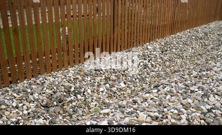 Il bordo del giardino presenta una nuova recinzione in legno accanto a un sentiero di ghiaia decorativa e piccoli ciottoli, creando un paesaggio pulito nel cortile Foto Stock