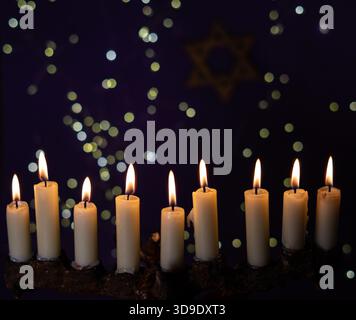 Una menorah con nove candele luminose è posta di fronte a una Stella di David su uno sfondo viola, che rappresenta Hanukkah Foto Stock