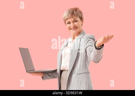 Donna d'affari matura con notebook su sfondo rosa Foto Stock