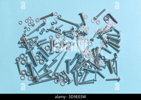 Diversi bulloni filettati e dadi cromati su sfondo blu Foto Stock