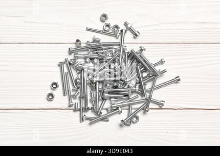 Pile di bulloni filettati e dadi cromati su fondo in legno bianco Foto Stock