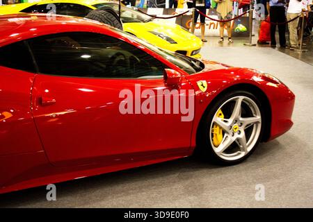 Un'auto sportiva Ferrari rossa brillante risplende sotto le luci di un salone di auto indoor, attirando l'attenzione con il suo design elegante e le pinze dei freni gialle. Foto Stock