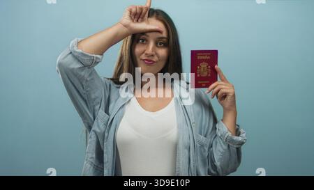 Donna in possesso di un passaporto spagnolo e che fa un cartello sulla fronte in blu studio; giocosa sicurezza di viaggio. Foto Stock
