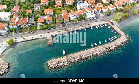 Vista aerea con droni di Marathias, un villaggio costiero della Grecia centrale, che mostra il porto, il mare cristallino, le case tradizionali e la strada principale. Foto Stock