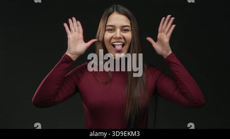 Donna sorridente e giocosa con una camicia marrone sullo sfondo nero, che esprime emozioni ed energia gioiose. Foto Stock