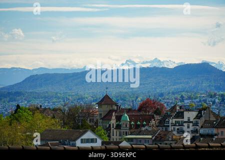 Vista panoramica della città con vista sui tetti piastrellati e gli edifici della città di Zurigo verso la maestosa catena montuosa delle Alpi svizzere innevate Foto Stock