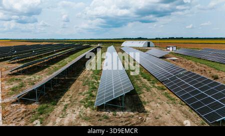 Vista aerea di file di pannelli solari che si estendono attraverso il paesaggio sotto un cielo punteggiato da nuvole soffici, creando un netto contrasto tra la tecnologia A. Foto Stock