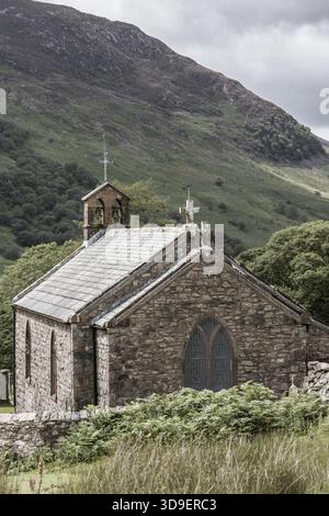 Vista della pittoresca cappella in pietra annidata in una valle con vegetazione verde e uno sfondo di maestose vette di montagna, Lake District, Inghilterra, United Ki Foto Stock
