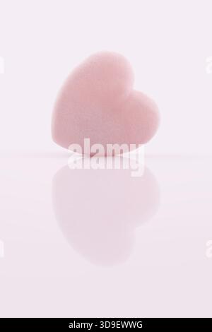 Un singolo soffice puff rosa a forma di cuore, adatto per l'applicazione di polvere, fondazioni o la rimozione del trucco. Il prodotto di bellezza è isolato su una superficie lucida Foto Stock