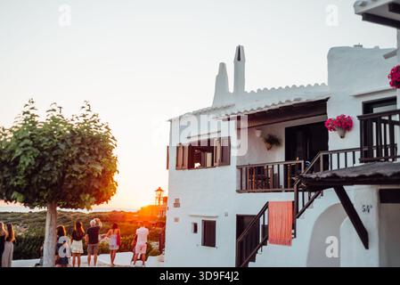 Persone che guardano il tramonto accanto alle case dipinte di bianco a Binibeca, Minorca Foto Stock