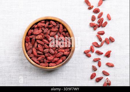 Bacche di goji essiccate, in una ciotola di legno su lino. Conosciuto anche come wolfberry cinese, medlar rosso e vitigno matrimoniale. Frutta dolce rossa-arancione brillante. Foto Stock