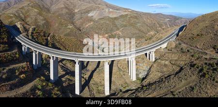 Veduta sopraelevata del viadotto autostradale A1 che attraversa il ripido e accidentato terreno di Kolsh nella contea di Kukës, circondato da colline color autunno e dal dr Foto Stock