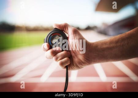Dettaglio di una persona con un cronometro in mano e una pista di atletica sullo sfondo. Foto Stock