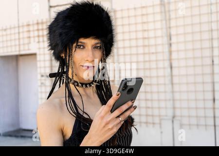 Giovane donna con uno stile di moda alternativo che usa il telefono cellulare. Persona alla moda che invia SMS o naviga Foto Stock