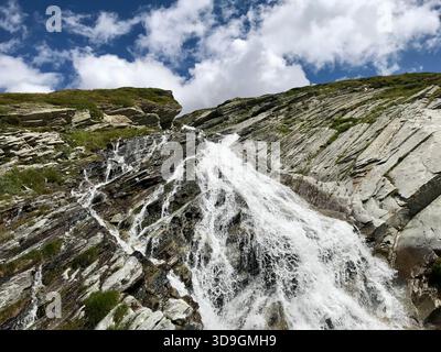 Il dinamico torrente di montagna scorre come una piccola cascata lungo un'imponente parete rocciosa presso il bacino idrico di Mattmark sopra SaaS-Fee, Vallese, Svizzera Foto Stock