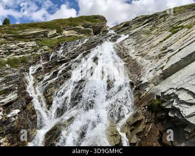 Il dinamico torrente di montagna scorre come una piccola cascata lungo un'imponente parete rocciosa presso il bacino idrico di Mattmark sopra SaaS-Fee, Vallese, Svizzera Foto Stock