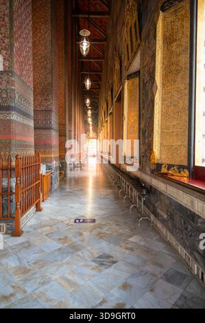 Corridoio illuminato dal sole all'interno della sala principale di Wat Pho a Bangkok, con pareti ornate a motivi geometrici e luce calda che scorre attraverso la porta, creando una pace Foto Stock