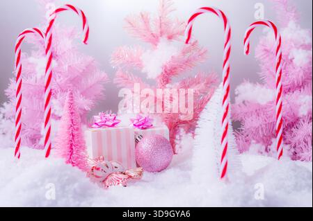 Una composizione natalizia rosa natalizia con scatole regalo rosa pastello, ornamenti scintillanti, decorazioni di caramelle e alberi in miniatura smerigliati. Foto Stock